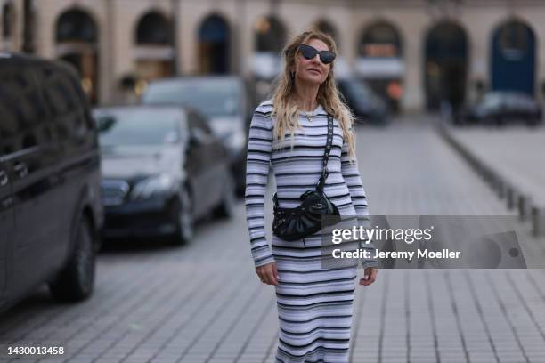 Sue Giers wearing SoSue striped knit dress, black Celine boots, Balenciaga le Cagole black bag, black Balenciaga shades during Paris Fashion Week on...