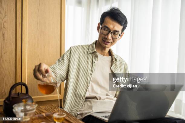 hombre asiático trabajando con una computadora portátil y bebiendo té - tea room fotografías e imágenes de stock