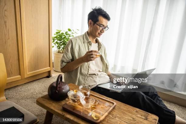asian man working with laptop and drinking tea - salão-de-chá imagens e fotografias de stock