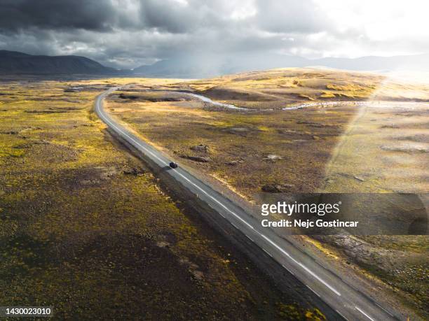 scenic view of a car driving on an empty road into the storm at sunset, aerial view with lens flare - car passion stock pictures, royalty-free photos & images