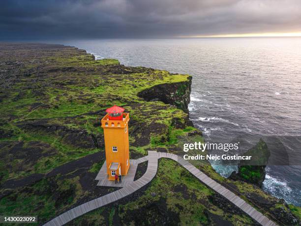 orange lighthouse on the edge of the black rock cliff at sunset - snaefellsnes bildbanksfoton och bilder