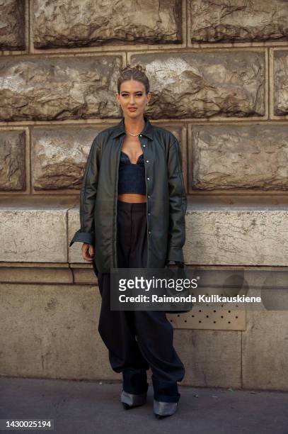 Emili Sindlev wearing wide navy blue jeans, blue denim crop top, dark green leather jacket, and black Loewe bag outside Loewe during Paris Fashion...