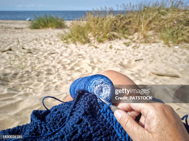 woman crocheting blue scarf on a beach. - crochet stock pictures, royalty-free photos & images