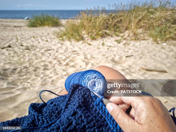 woman crocheting blue scarf on a beach. - knitting stock pictures, royalty-free photos & images