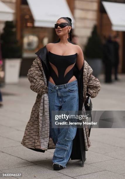 Sofia Ghasab is seen wearing gold earrings, black Balenciaga sunglasses, black transparent Mugler top/body, blue denim wide leg cargo pants, beige...