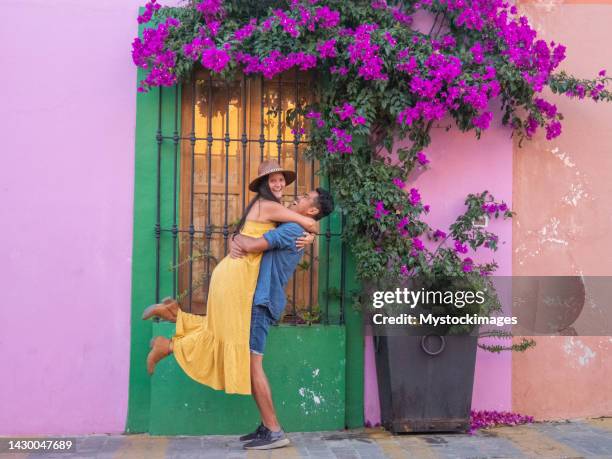 multiracial couple traveling in mexico and posing under a bougainvillea tree - woman wearing purple dress stock pictures, royalty-free photos & images