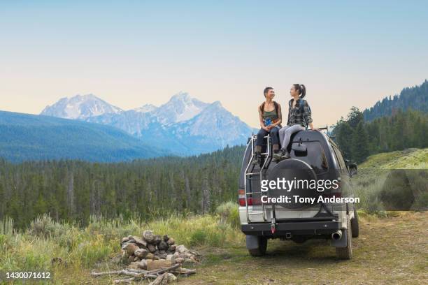 two young woman on top of camper van in remote mountain landscape - camping couple stockfoto's en -beelden