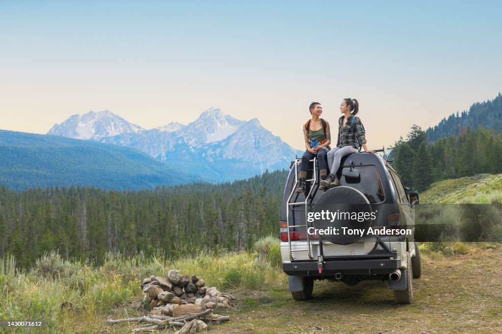 Two young woman on top of camper van in remote mountain landscape
