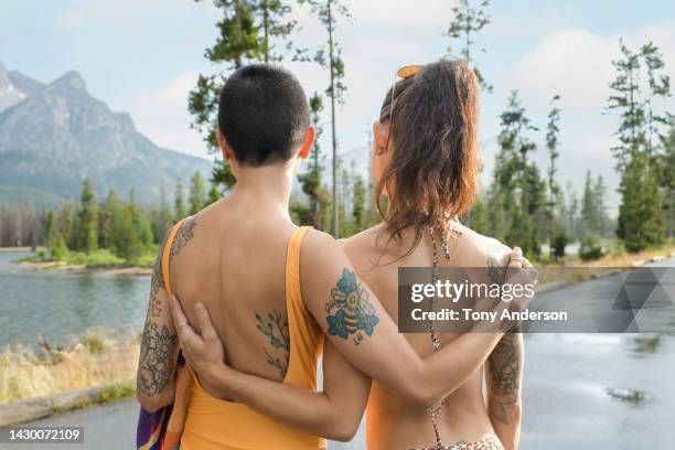 two young woman embracing at mountain lake - landscape tattoo stock pictures, royalty-free photos & images