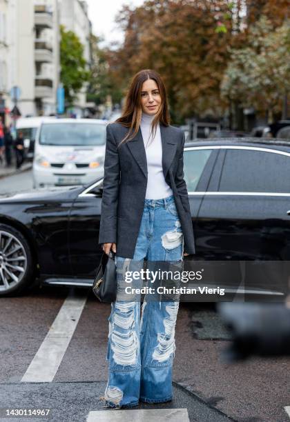 Gala Gonzalez wears destroyed ripped denim jeans, black blazer, white turtleneck, bag outside Givenchy during Paris Fashion Week - Womenswear...