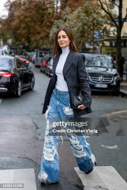 Gala Gonzalez wears destroyed ripped denim jeans, black blazer, white turtleneck, bag outside Givenchy during Paris Fashion Week - Womenswear...