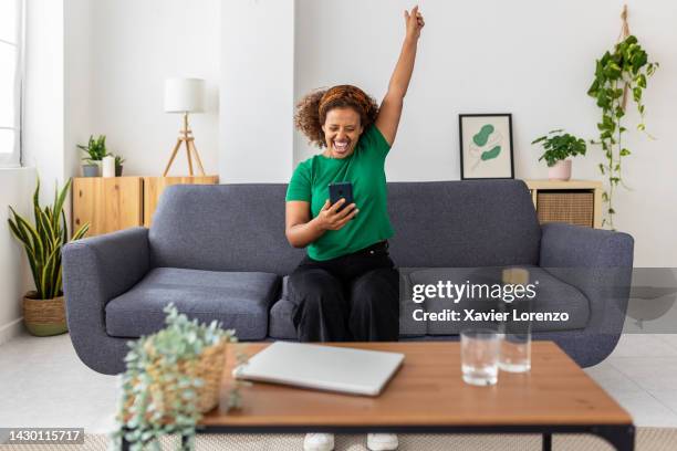 excited young african woman celebrating success looking mobile phone screen - winner stockfoto's en -beelden