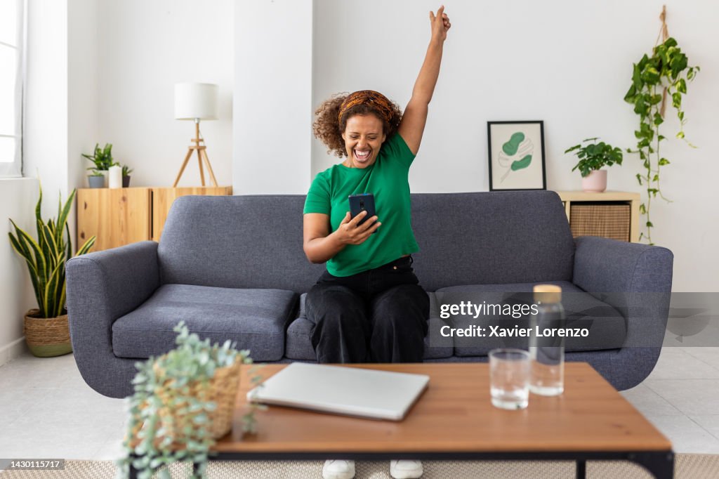 Excited young african woman celebrating success looking mobile phone screen