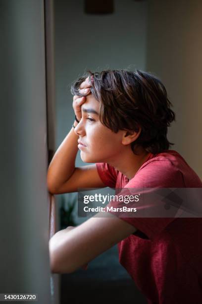sad, worried pre adolescent boy looking out the window - lockdown loneliness stock pictures, royalty-free photos & images