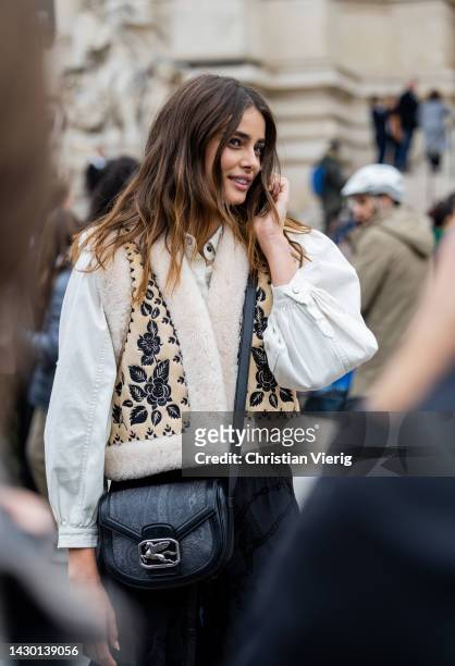 Model Taylor Hill wears white blouse, beige vest, black ruffled bag, ruffled pants outside Zimmermann during Paris Fashion Week - Womenswear...