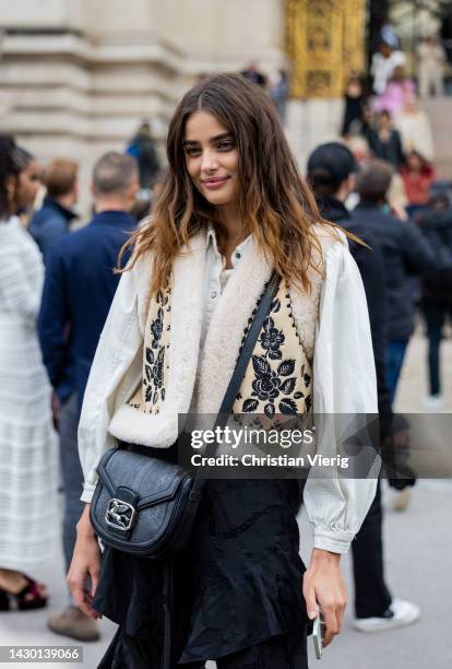 Model Taylor Hill wears white blouse, beige vest, black ruffled bag, ruffled pants outside Zimmermann during Paris Fashion Week - Womenswear...