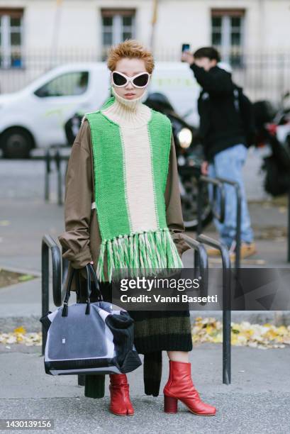 Guest poses wearing Margiela red tibi ankle boots and Balenciaga sunglasses after the Sacai show during Paris Fashion Week - Womenswear Spring/Summer...