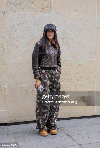 Yoyo Cao wears flat cap, brown leather jacket, pants with print outside Stella McCartney during Paris Fashion Week - Womenswear Spring/Summer 2023 :...