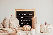 Felt letter board and text let our lives be full of thanks and giving. Autumn table decoration. Interior decor for thanksgiving and fall holidays with handmade pumpkins and candles