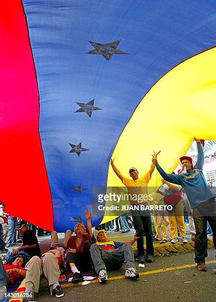 Supporters of Venezuelan President Hugo Chavez sit under a giant flag during a march in Caracas, 29 July 2002. Thousands of Chavez supporters...