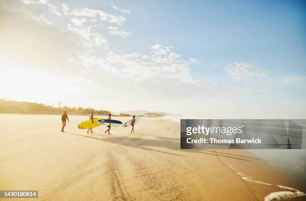 wide shot of family carrying surfboards while taking surf lesson - travel stock-fotos und bilder
