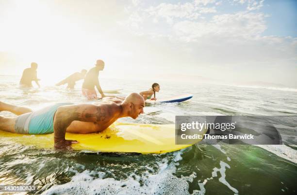 wide shot of father paddling out on surfboard during lesson - taking a shot - sport imagens e fotografias de stock