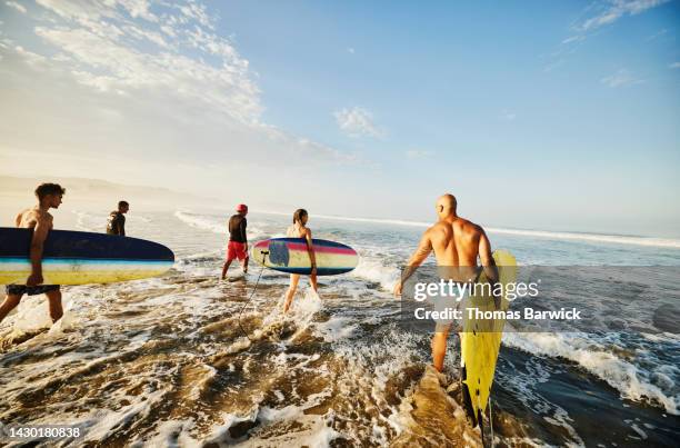 wide shot of family carrying surfboards into ocean during surf lesson - バハカリフォルニア ストックフォトと画像