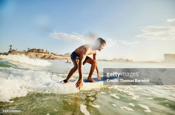 wide shot of teenage boy riding wave while taking surf lesson - taking a shot - sport imagens e fotografias de stock