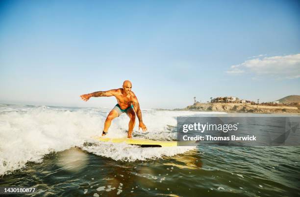 wide shot of smiling man riding wave while taking surf lesson - ride the wild surf stock pictures, royalty-free photos & images