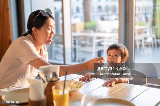mother feeding her baby boy in the restaurant with macaroni and cheese - asian spoon feeding happy stock pictures, royalty-free photos & images