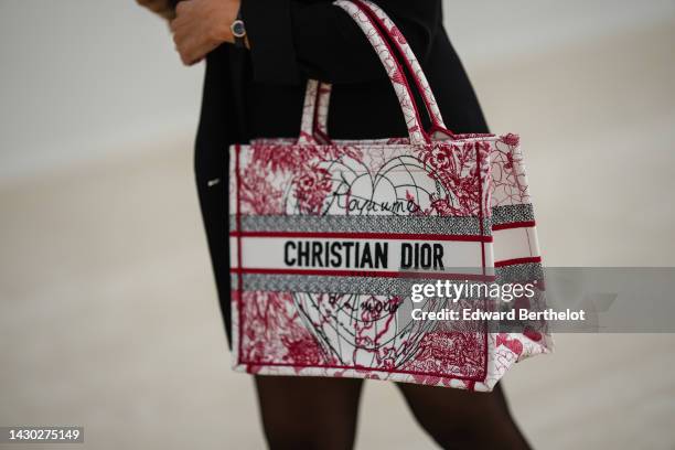 Guest wears black pants, a white with red and black embroidered pattern Book Tote handbag from Dior, outside Dior, during Paris Fashion Week -...