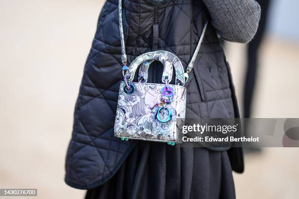 Guest wears a gray wool pullover, a black quilted sleeveless jacket from Dior, a black pleated long skirt, a white and black embroidered print...