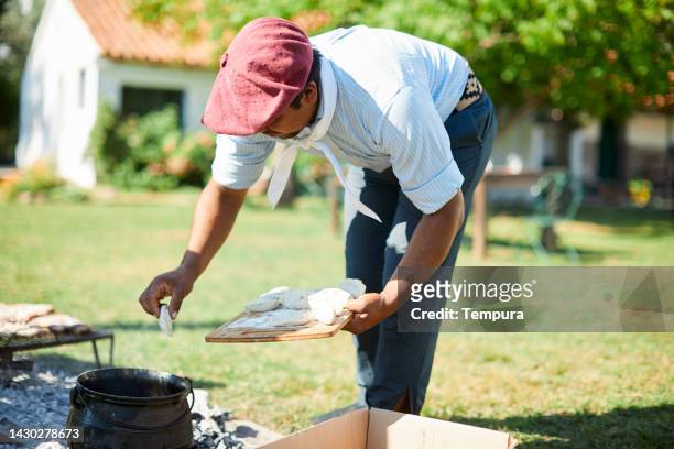 gaucho rüde bereitet das fleisch auf dem grill mit bauernhaus im hintergrund zu - pampa argentine stock-fotos und bilder