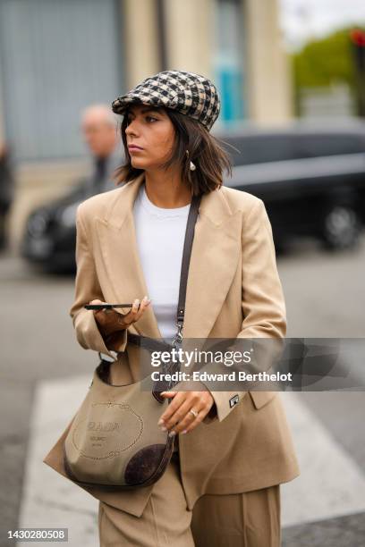 Guest wears a beige and black houndstooth print pattern wool beret, a white t-shirt, pearls pendant earrings, a beige blazer jacket, beige large...