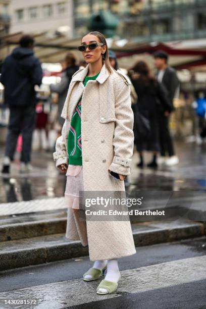 Guest wears a brown sunglasses, silver and black earrings, a green with pale pink print pattern wool pullover, a beige embossed pattern long coat, a...