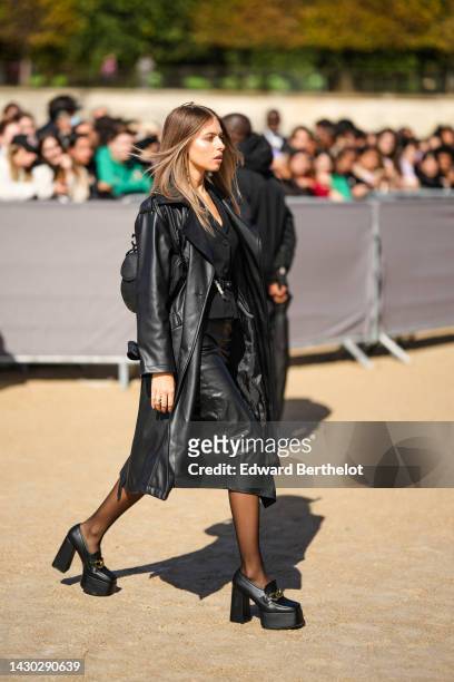 Guest wears a black buttoned jacket, a black shiny leather long coat, a black shiny leather midi skirt, black tights, a black shiny leather Saddle...