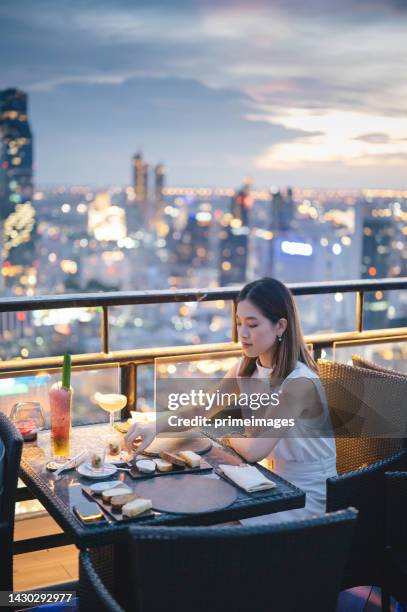 freunde treffen sich und trinken gemeinsam cocktails im wolkenkratzer-dachrestaurant in metropole bei sommersonnenuntergang. - asian restaurant stock-fotos und bilder