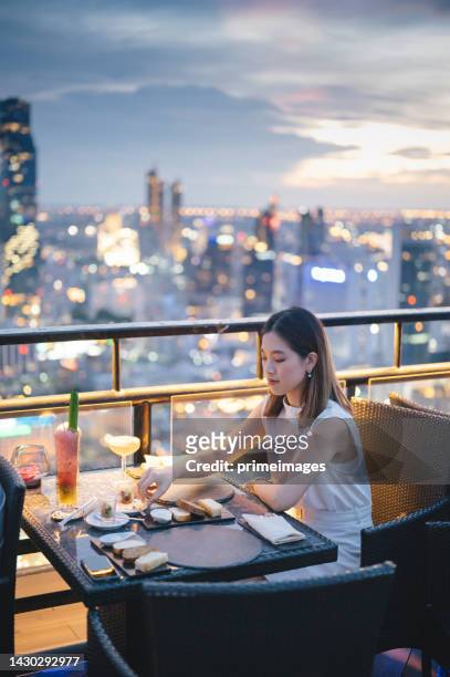 friends meeting and drinking cocktail together at skyscraper rooftop restaurant in metropolis at summer sunset. - dining stock pictures, royalty-free photos & images