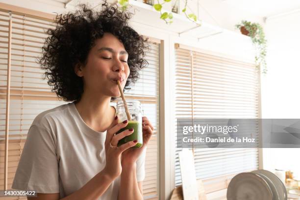 young mixed race black latina woman drinking healthy green juice with bamboo straw. copy space. healthy lifestyle - smoothie bildbanksfoton och bilder