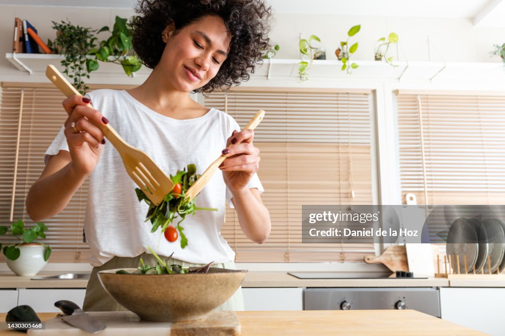 Happy young multiracial woman mixing bowl of fresh salad. Copy space.Healthy lifestyle