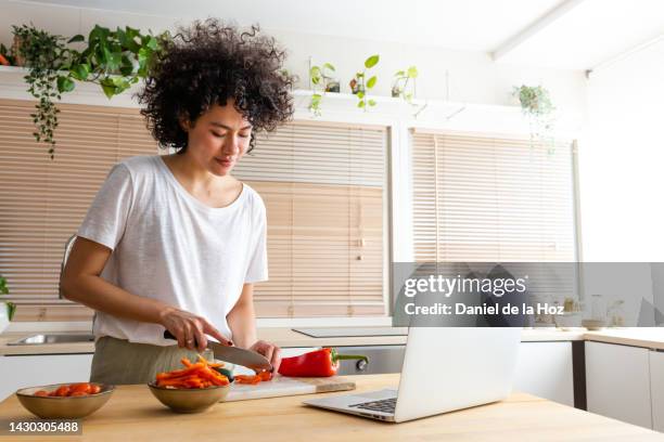 young african american woman cooking following online recipe using laptop to read ebook at home kitchen. cutting peppers. copy space. technology - mujer cocinando fotografías e imágenes de stock