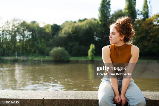 woman sat on wall next to river - mental wellbeing stock pictures, royalty-free photos & images