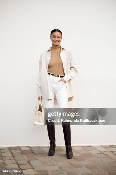 Guest wearing white pants, a beige turtle neck top, a white shirt, a white Hermes bag, and black heel boots outside the Hermes show during Paris...