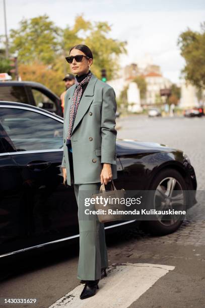 Julia Haghjoo wearing black sunglasses, a black turtleneck top, a navy blue with camel and white print pattern silk scarf, a gray-green blazer,...