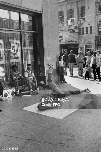 Small crowd gathers to watch as a youth windmills on a piece of linoleum, as three others watch as the sit with a boombox in Times Square, in the...