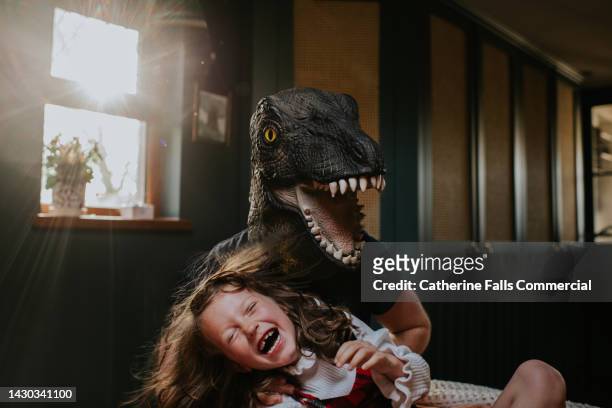 playful image of a father playing with his little girl. he wears a rubber dinosaur mask. she squeals with delight. - vrijetijd sport en spel stockfoto's en -beelden