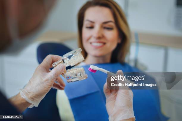 dentist with protective face mask showing patient how to brush teeth on plastic model. - preventive care stock pictures, royalty-free photos & images