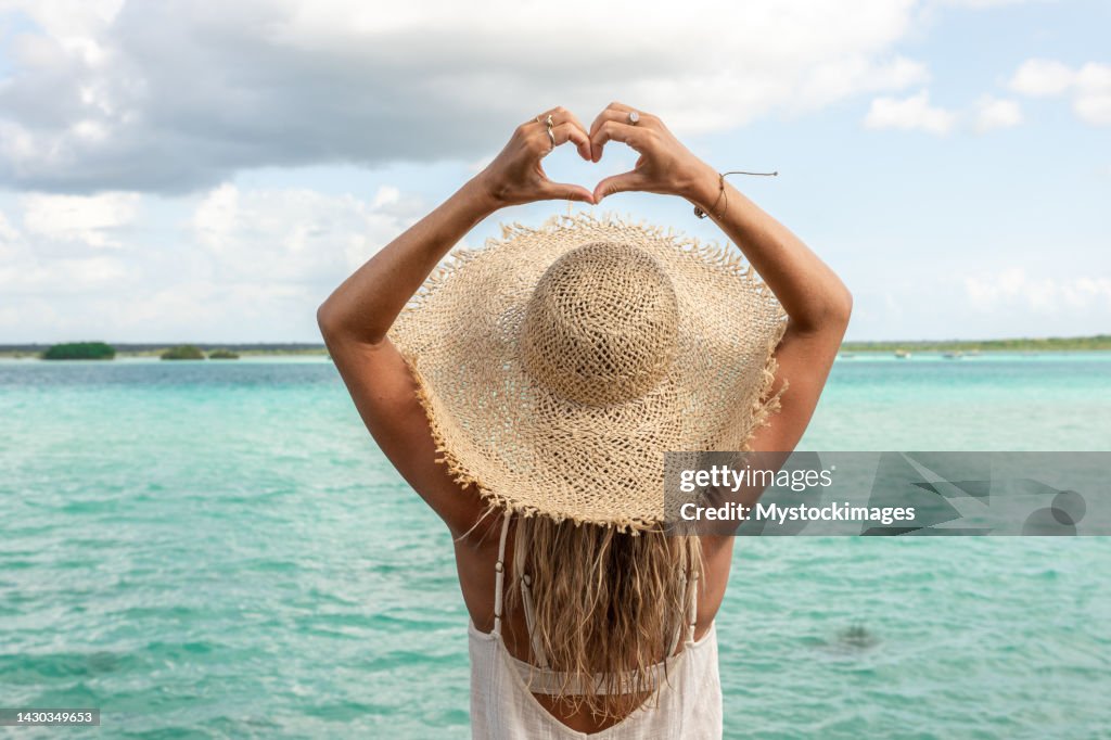 Young woman on a treehouse above a beautiful lagoon makes heart with hands
