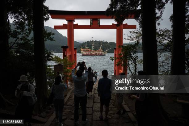 Tourists take photographs of a pirate ship cruise sailing on Ashinoko Lake through the Torii of Peace at Hakone Shrine on October 04, 2022 in Hakone,...