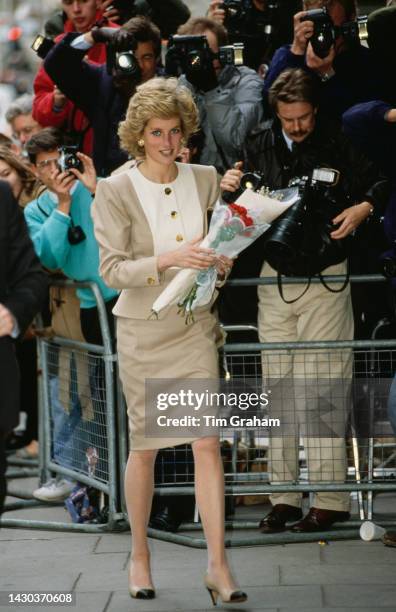 Princess Diana wearing a beige-and-white suit by Catherine Walker, walks past crowd holding a bouquet of flowers at King Edward VII's Hospital Sister...